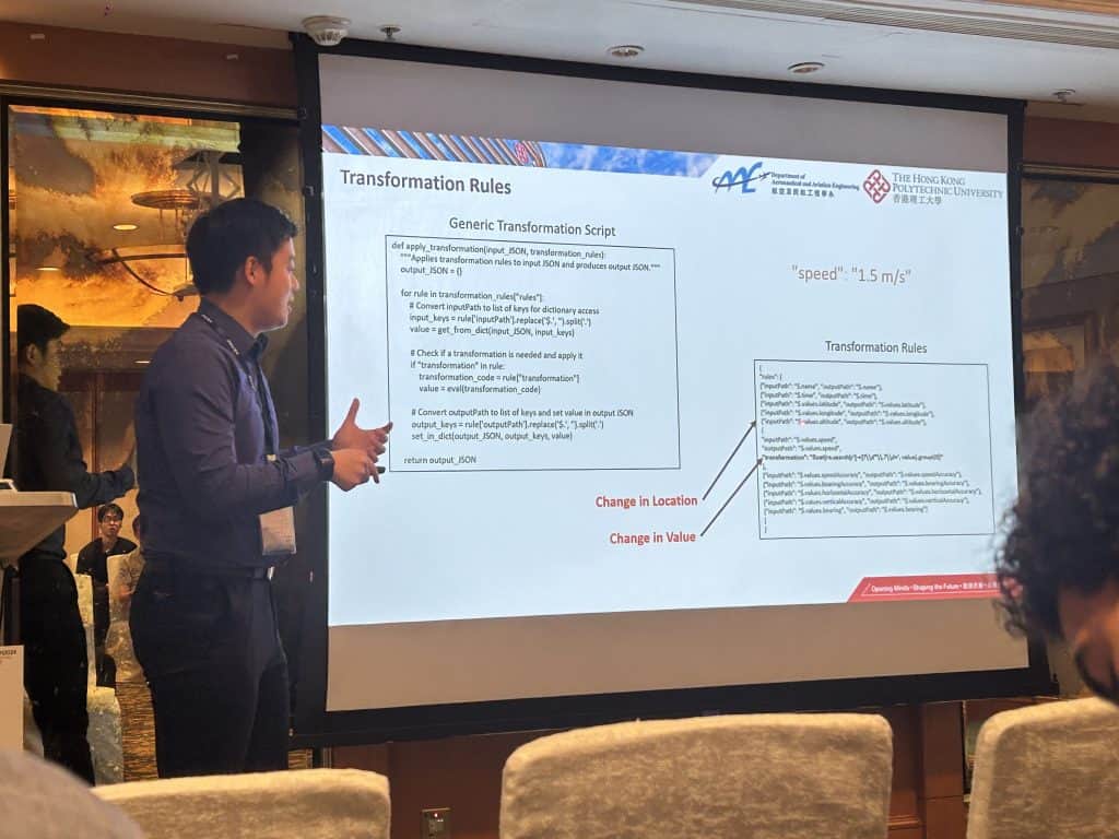 Ju Lin presenting at a lectern beside a projected slide titled Transformation Rules, showing the transformation script and the JSON it rewrites